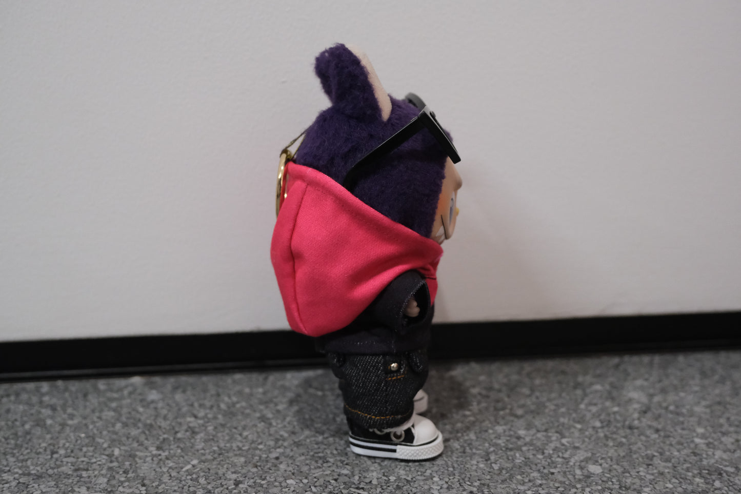 A Labubu figure from the side, wearing a pink and black hoodie that shows the color blocking detail, paired with dark denim shorts.