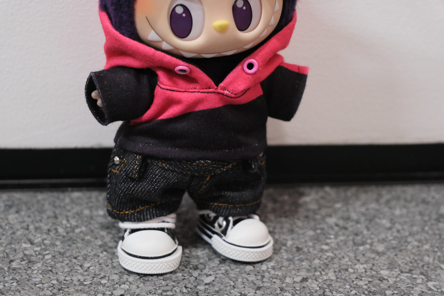 Close-up shot of a Labubu figure showing the details of the pink and black color-blocked hoodie layered over its body, and the texture of the dark denim shorts.