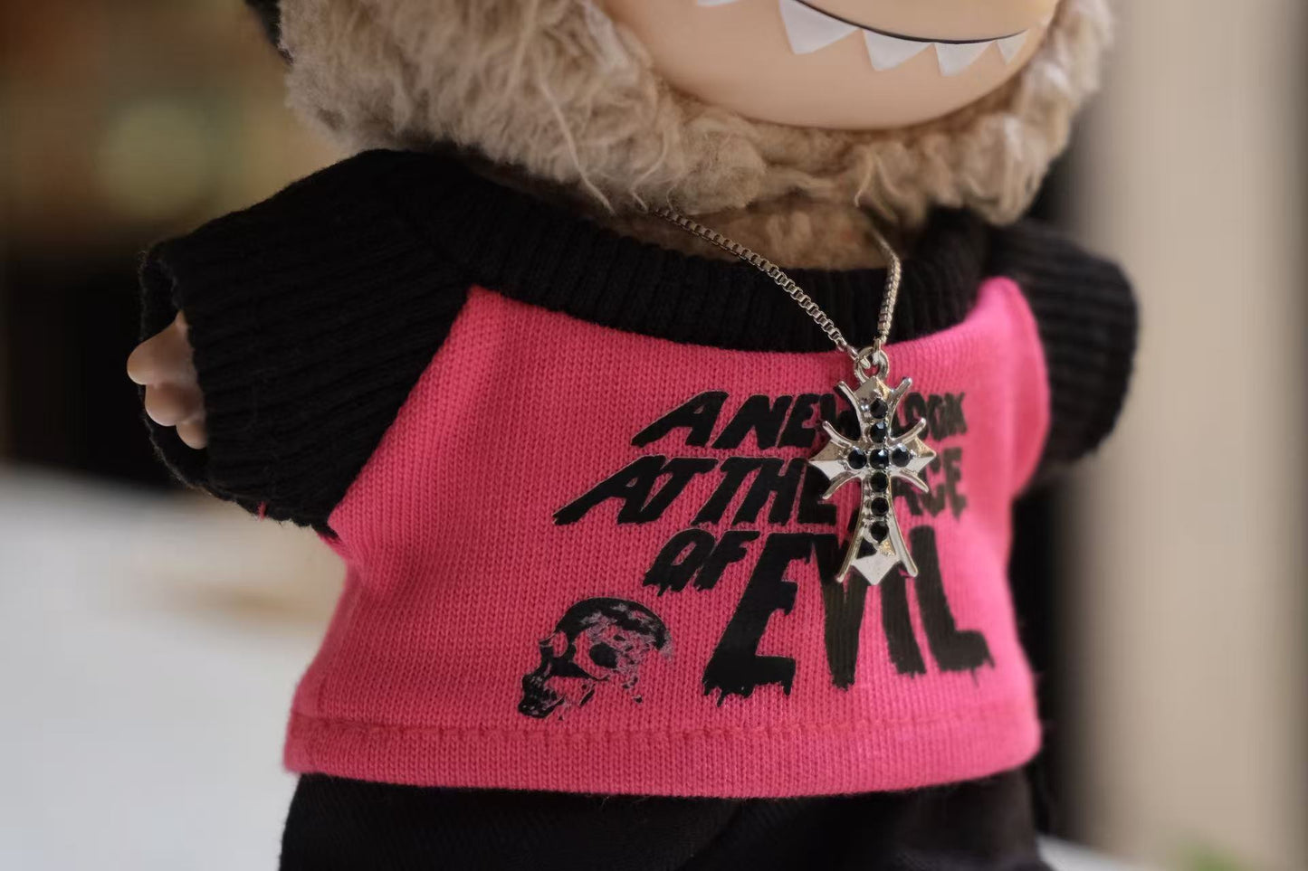 Close-up of The labubu figure's black pink t-shirt and cross necklace