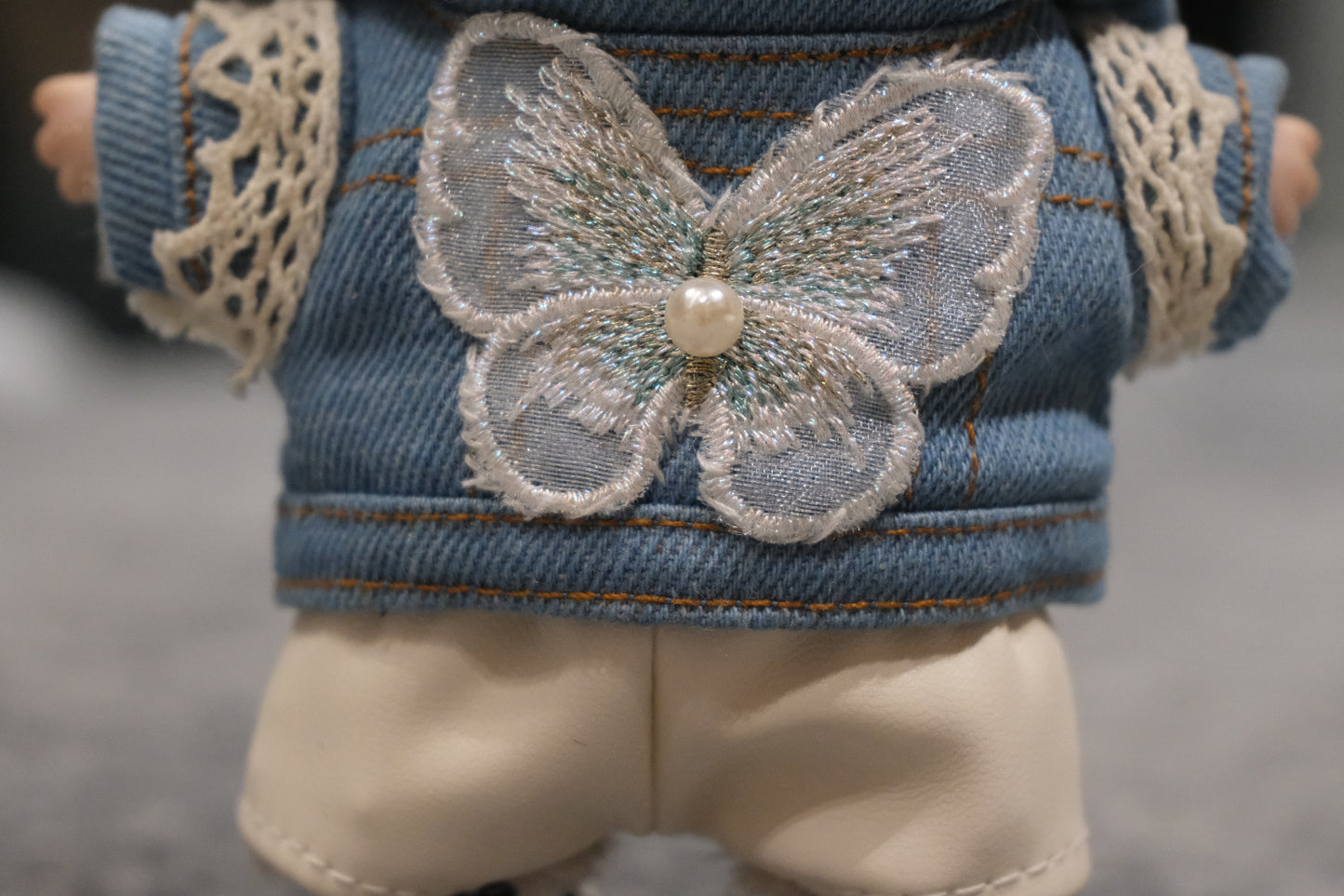 Close-up of The labubu figure's denim jacket with an embroidered butterfly patch and pearl detail.
