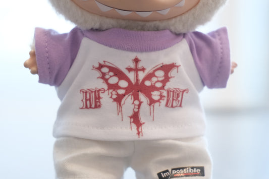 a close up of Labubu figure wearing a white and purple gothic butterfly graphic t-shirt