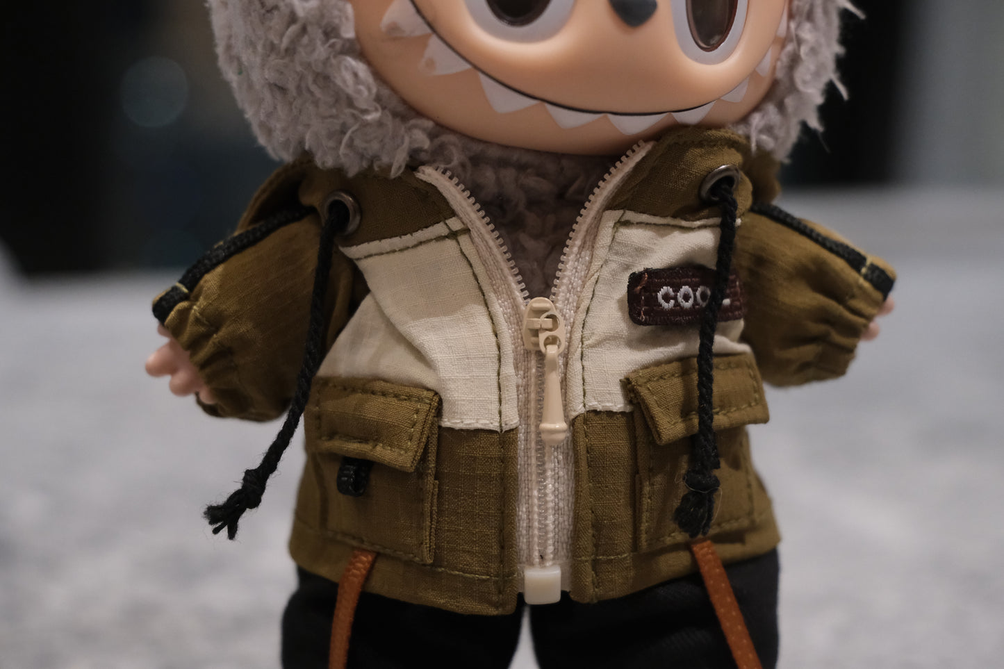 Close-up of The labubu figure's khaki utility jacket with "COOL" patch and pockets.