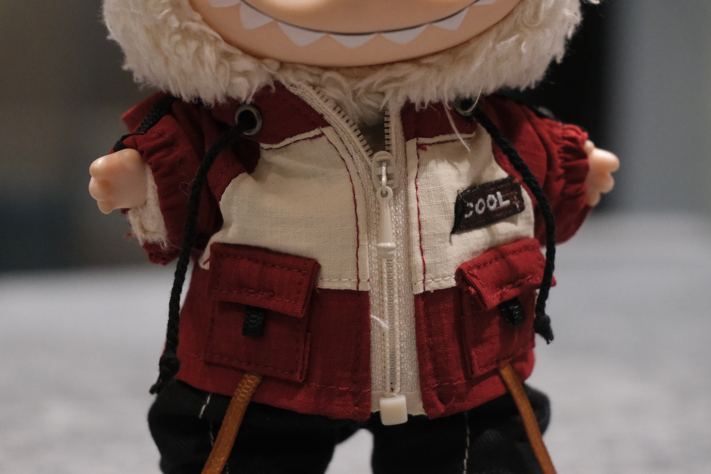 Close-up of The labubu figure's khaki utility jacket with "COOL" patch and pockets.