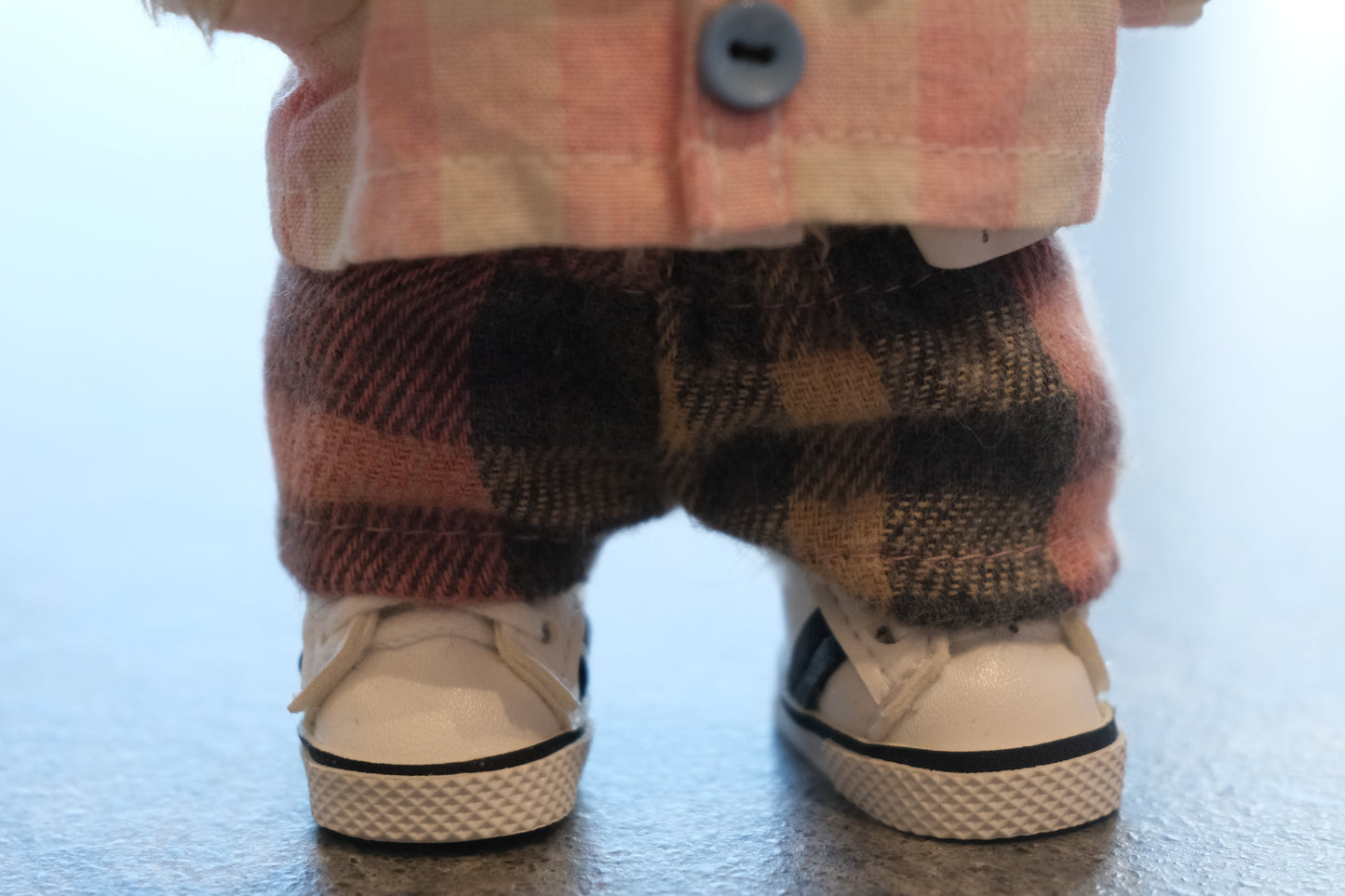 Close-up of The labubu figure's pink gingham shirt, mismatched buttons, and cozy flannel pants