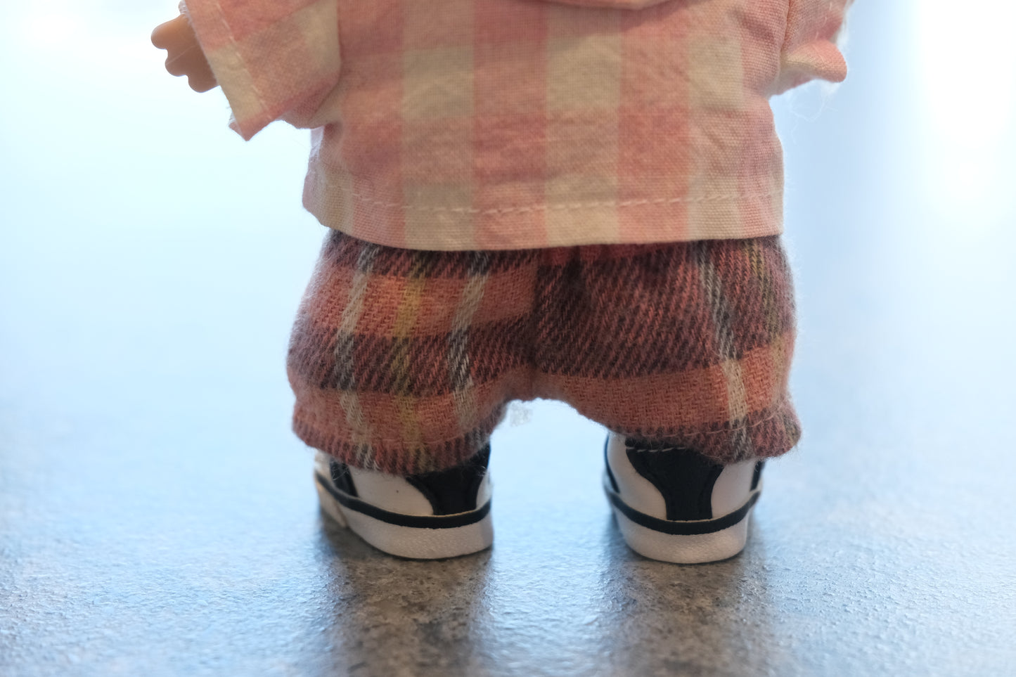 Close-up of The labubu figure's pink gingham shirt, mismatched buttons, and cozy flannel pants