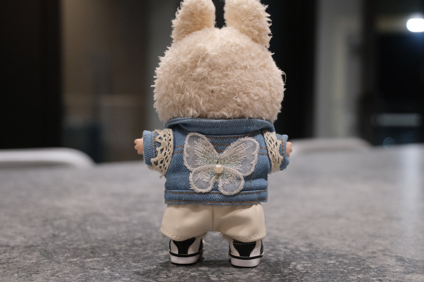 Labubu figure wearing a 5-piece outfit: light blue denim jacket, white tee, white leather shorts, sun necklace, and sneakers.
