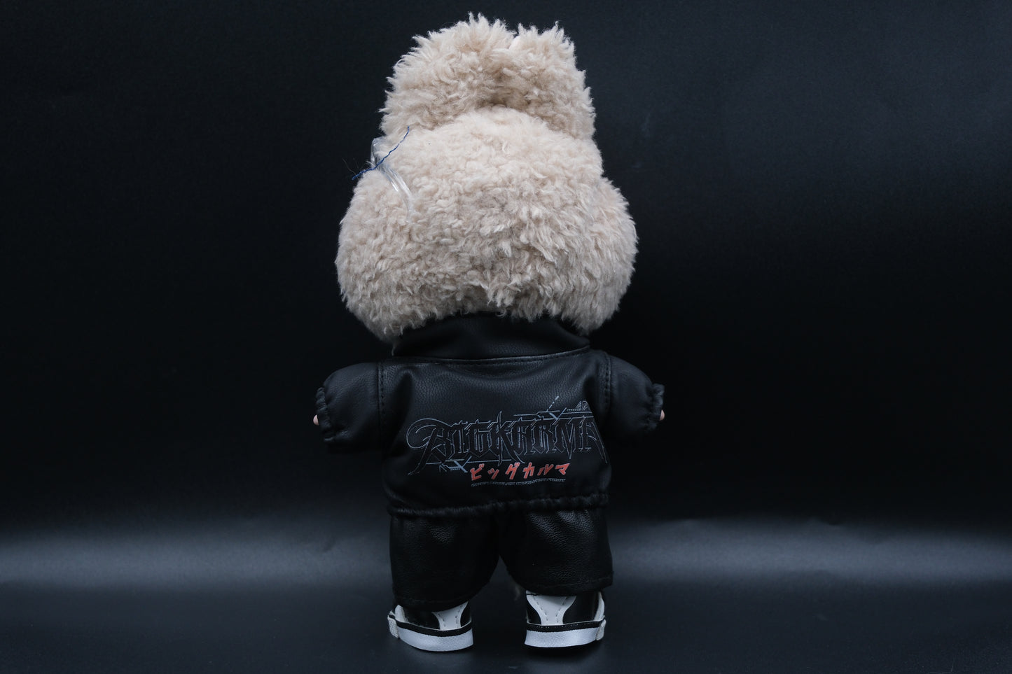 A back view of Labubu designer toy figure in a dark, urban-style outfit, featuring a black leather jacket and pants , sunglasses and a pair of shoes