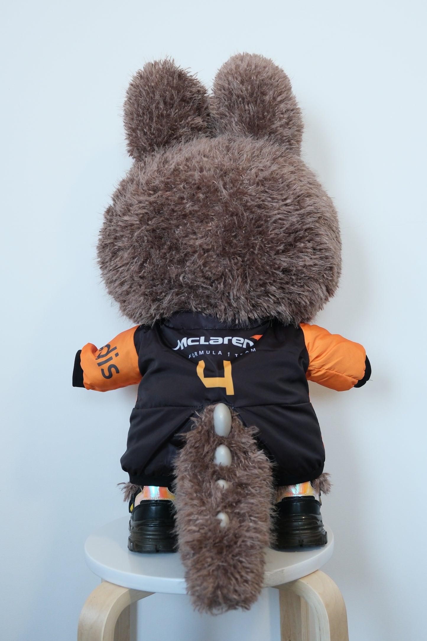 back view of 58cm Mega Zimomo wearing a McLaren F1 racing jumpsuit in orange and black