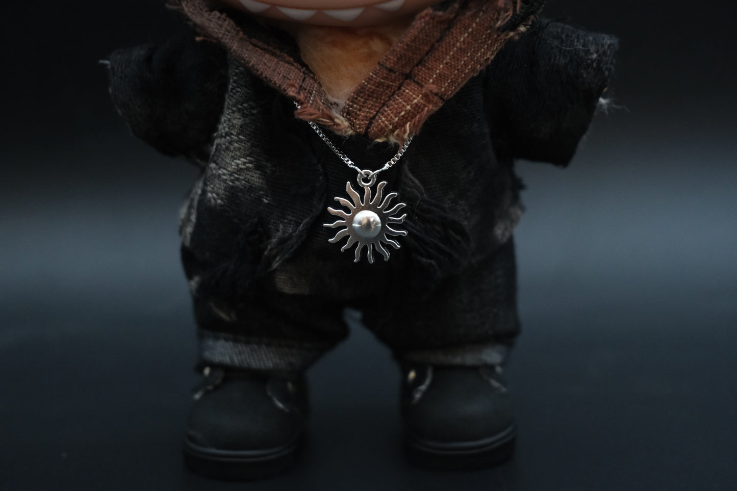 Close-up of the sun pendant necklace and the rough, distressed fabric of the hoodie
