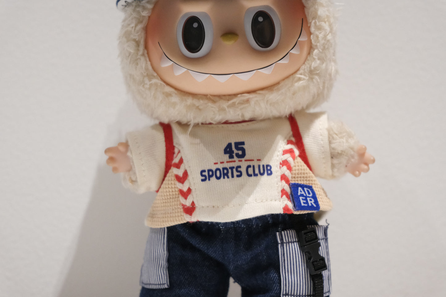 Close-up of The labubu figure's distressed denim cap and graphic t-shirt