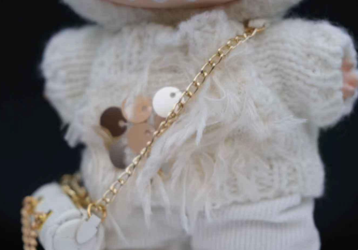 Close-up of a labubu wearing a white knitted outfit with a gold chain and pearl detail.