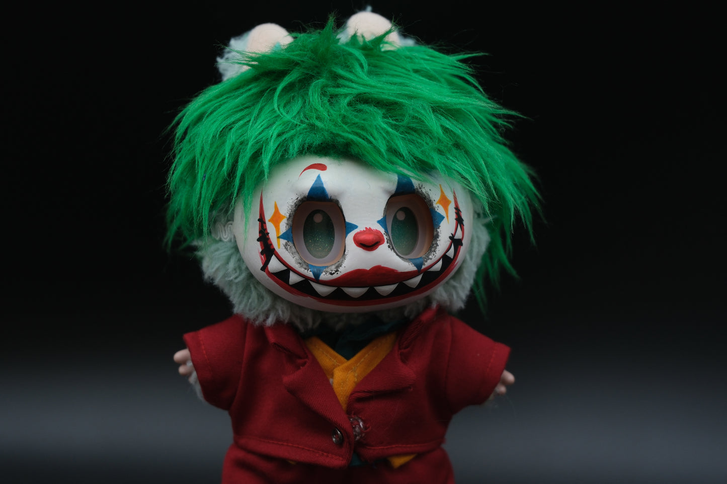 Close-up of The labubu figure's red suit jacket, shirt, green wig, mask and orange vest