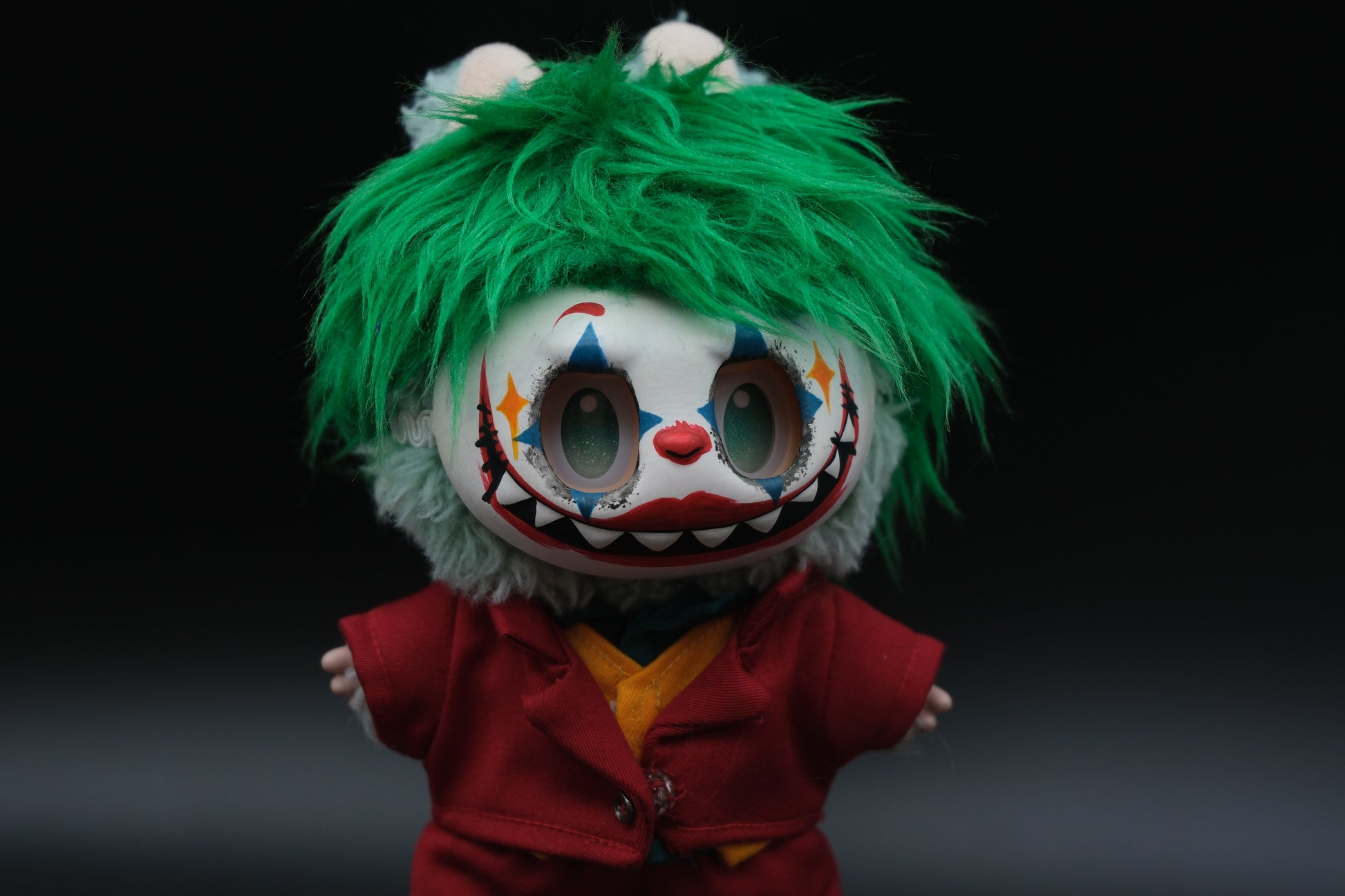 Close-up of The labubu figure's red suit jacket,  shirt, green wig, mask and orange vest