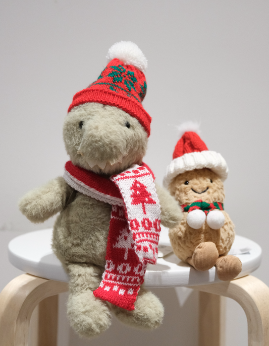 Two-piece festive accessory set for Jellycat Dinosaur, featuring a red Santa hat and miniature red scarf laid flat.