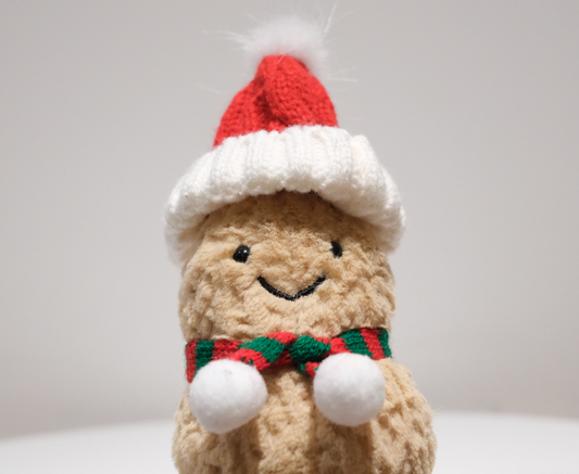 Close-up of the miniature Santa hat and knit scarf detail on the Jellycat Amuseables Peanut plush.
