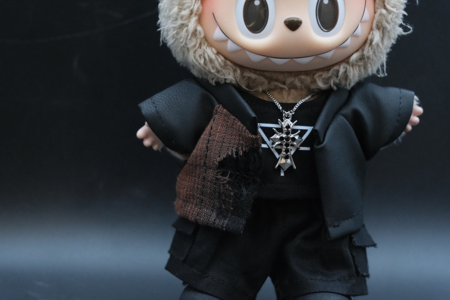 Close-up of a Labubu figure showing the details of the black embossed jacket, black t-shirt, checkered pants, and a unique pearl necklace.