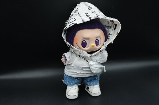 A Labubu figure from the side, showcasing the distressed white hooded jacket with black lettering and graphics on the hood, the layered white top, and the distressed blue denim shorts.
