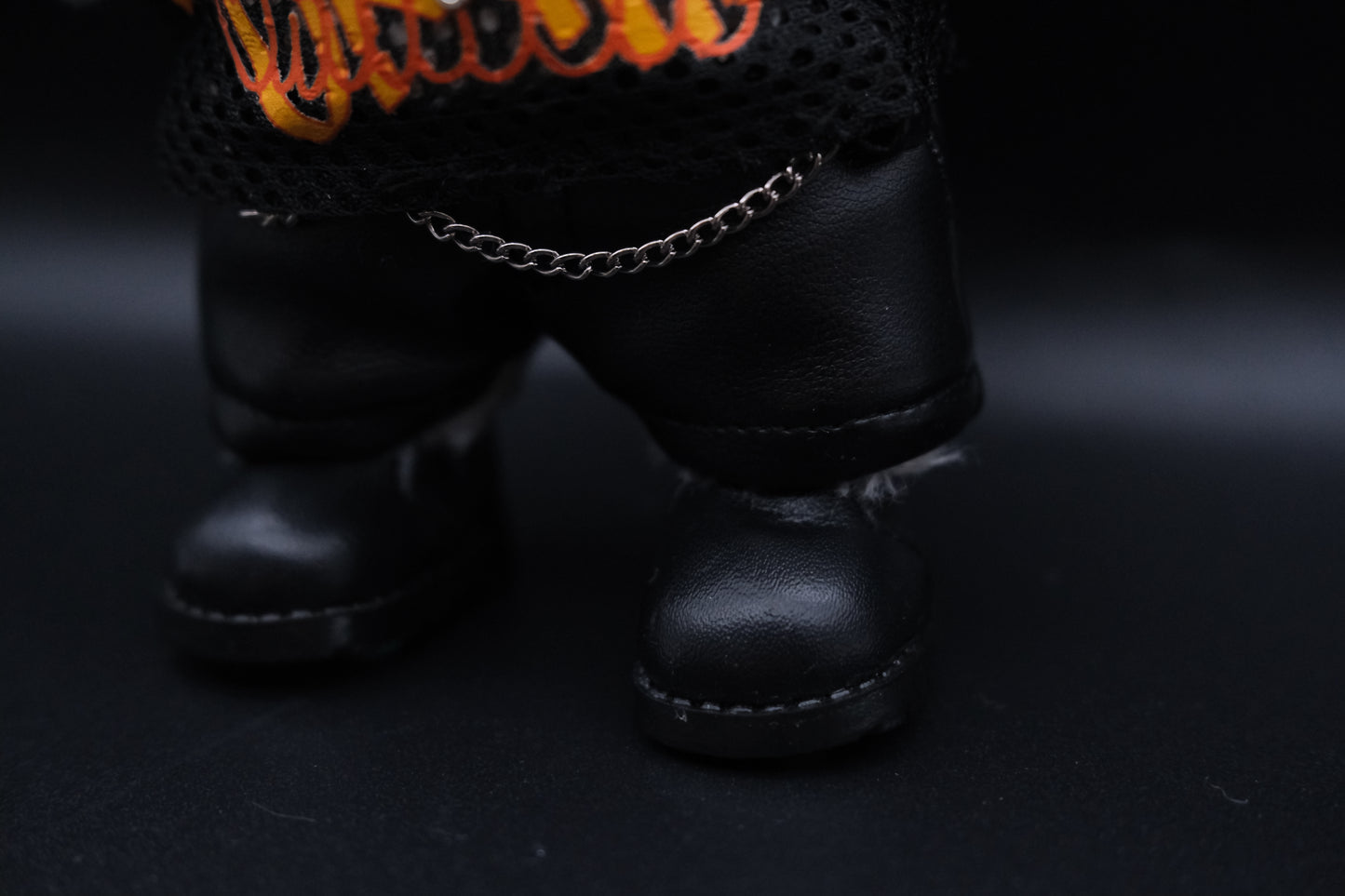details of a labubu mesh shirt, leather pants, black shoes and cross necklace