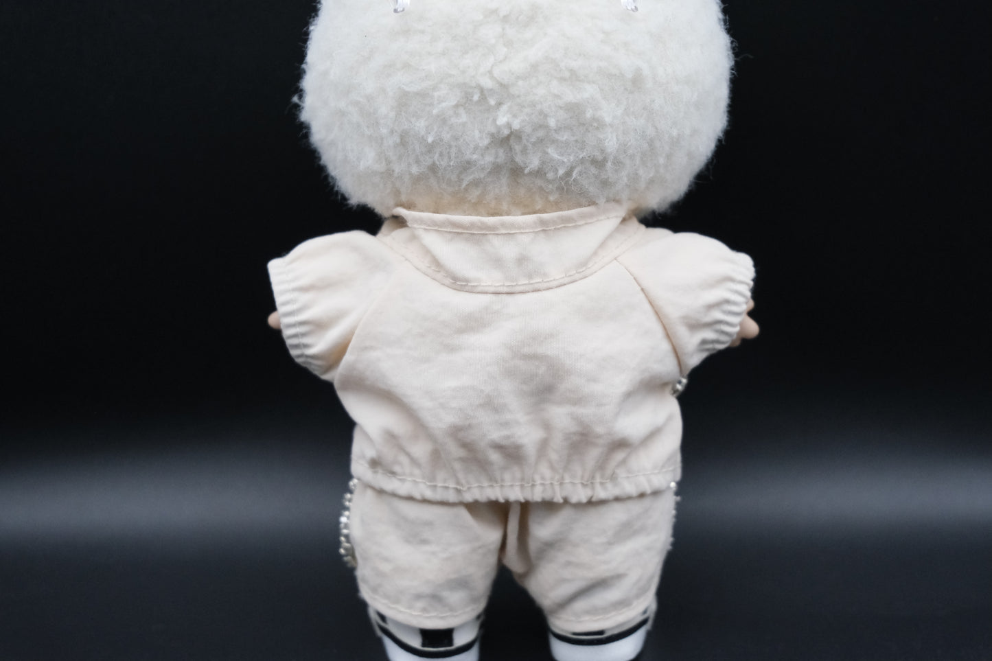 back view of A Labubu figure wearing a white zippered jacket, white pants and and white sneakers.