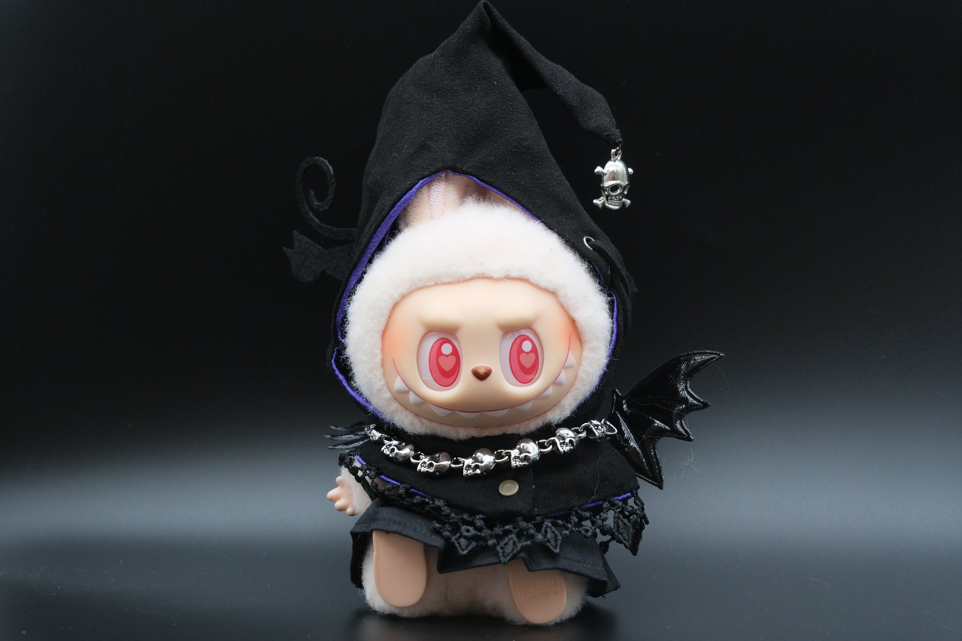 A Labubu figure wearing a 4-piece spooky streetwear outfit, including a black hoodie, a white dress, and a pumpkin mask.