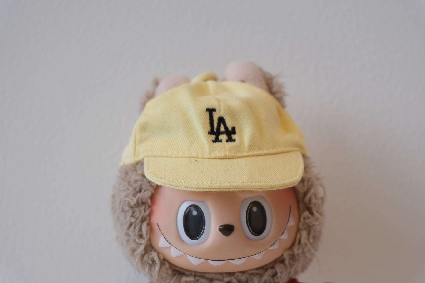labubu with a yellow cap featuring the LA logo on a plain background