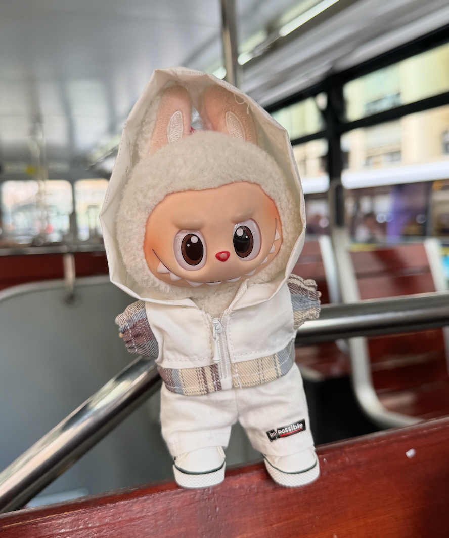 A trendy Labubu designer toy figure wearing a minimalist white zip-up hoodie with a contrasting white zipper, white pants, and stylish white high-top sneakers with black accents.