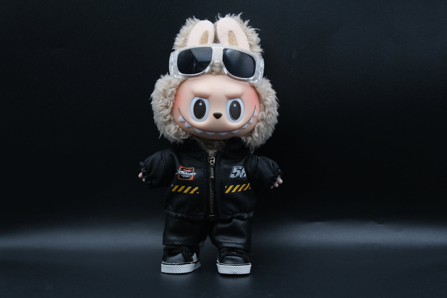 A Labubu designer toy figure in a dark, urban-style outfit, featuring a black leather jacket and pants , sunglasses and a pair of shoes