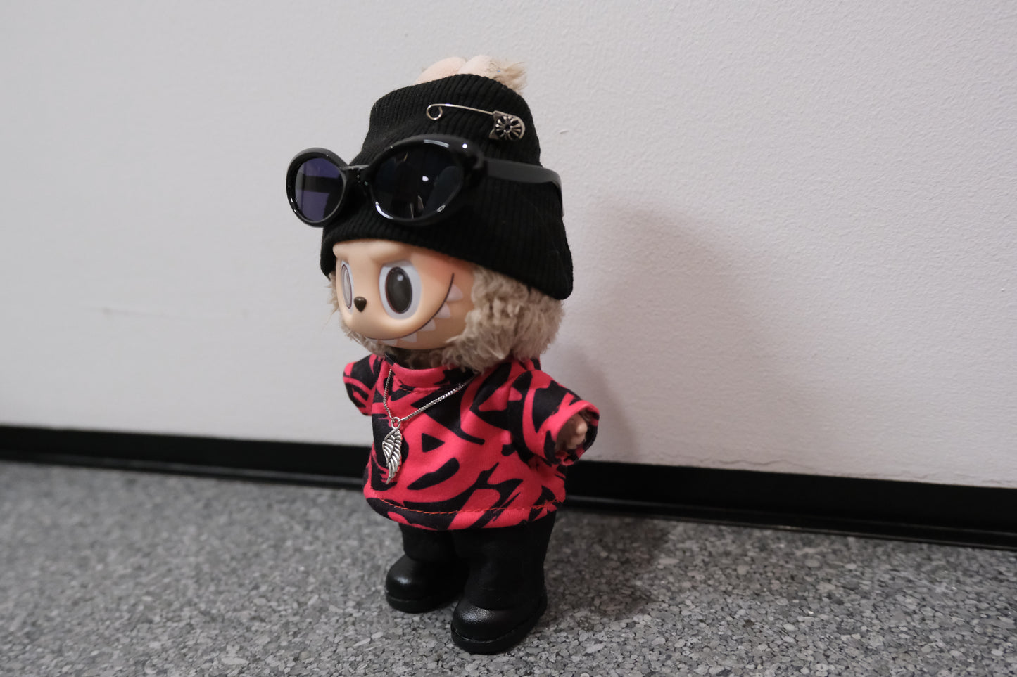 labubu wearing a black cap, sunglasses, and a red and black patterned t-shirt