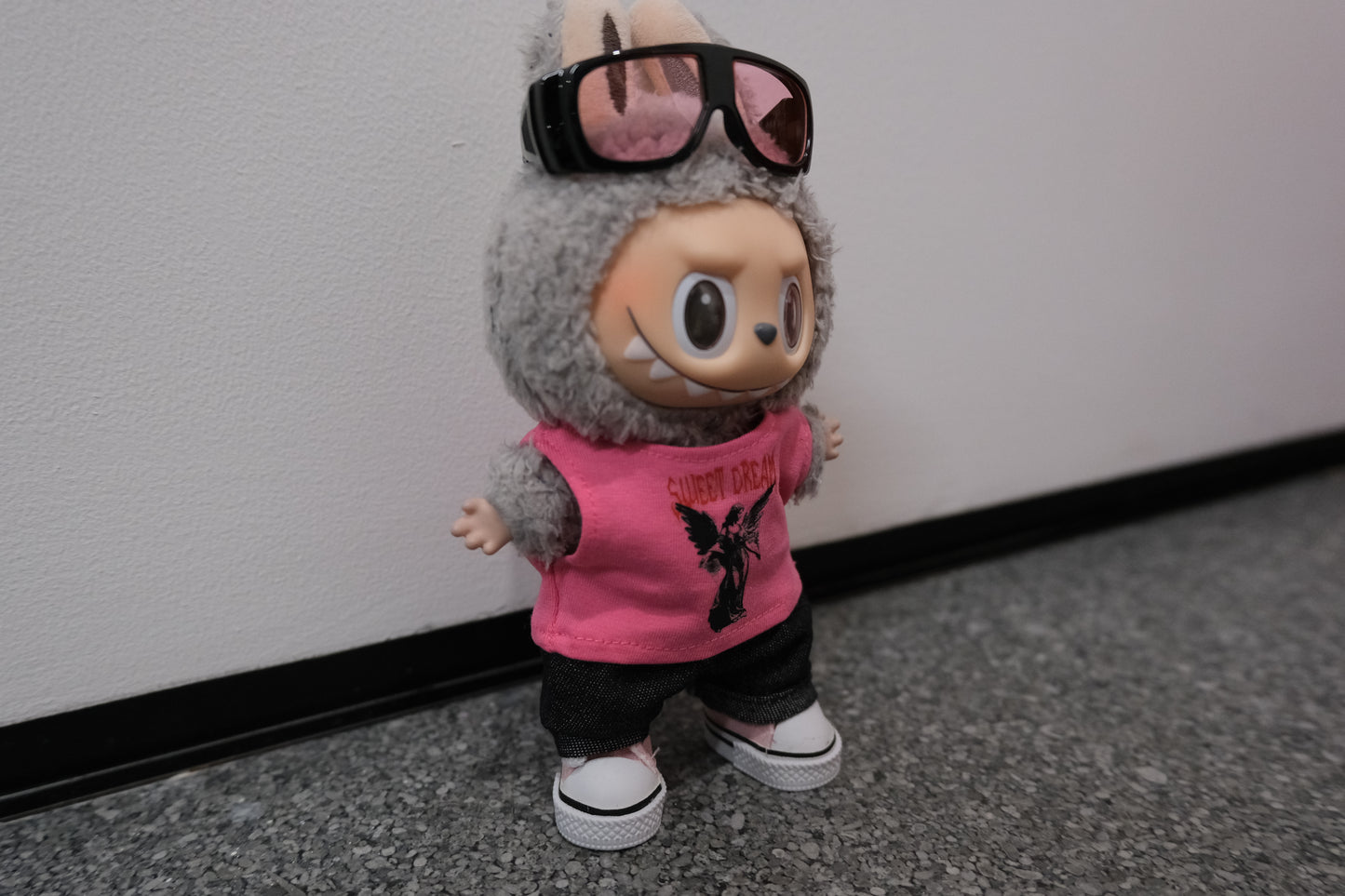 A Labubu figure wearing a 4-piece modern casual outfit, including a pink vest, denim jeans, sunglasses with a metallic frame, and pink sneakers.