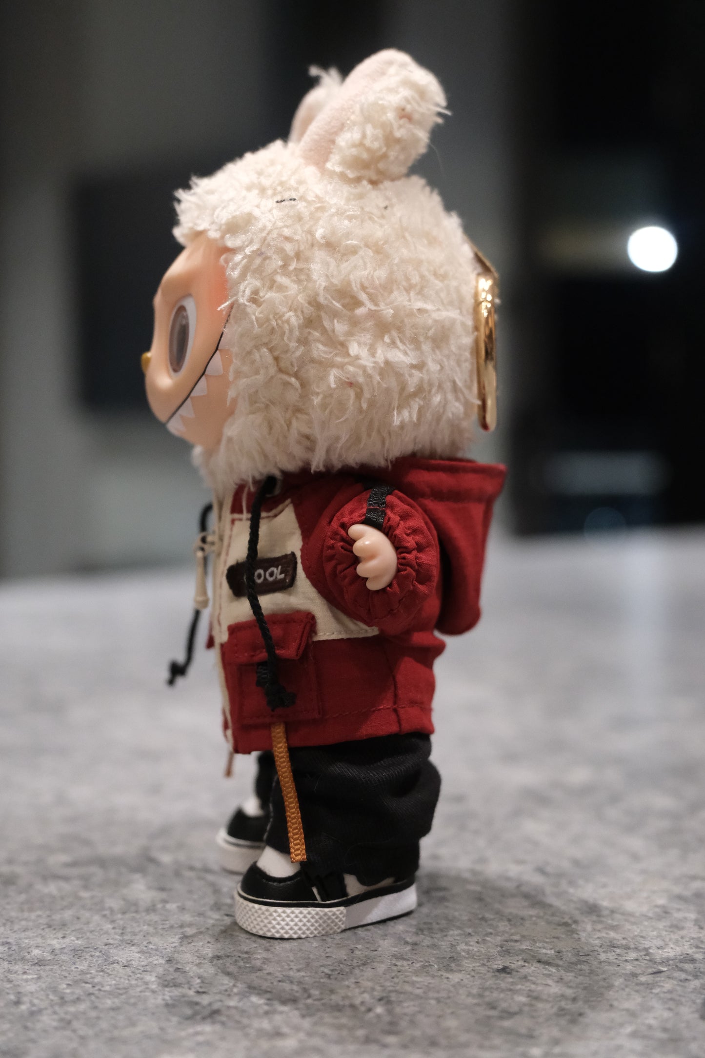 side view of Labubu figure wearing a red and white mountaineering parka jacket, black pants, and black sneakers.