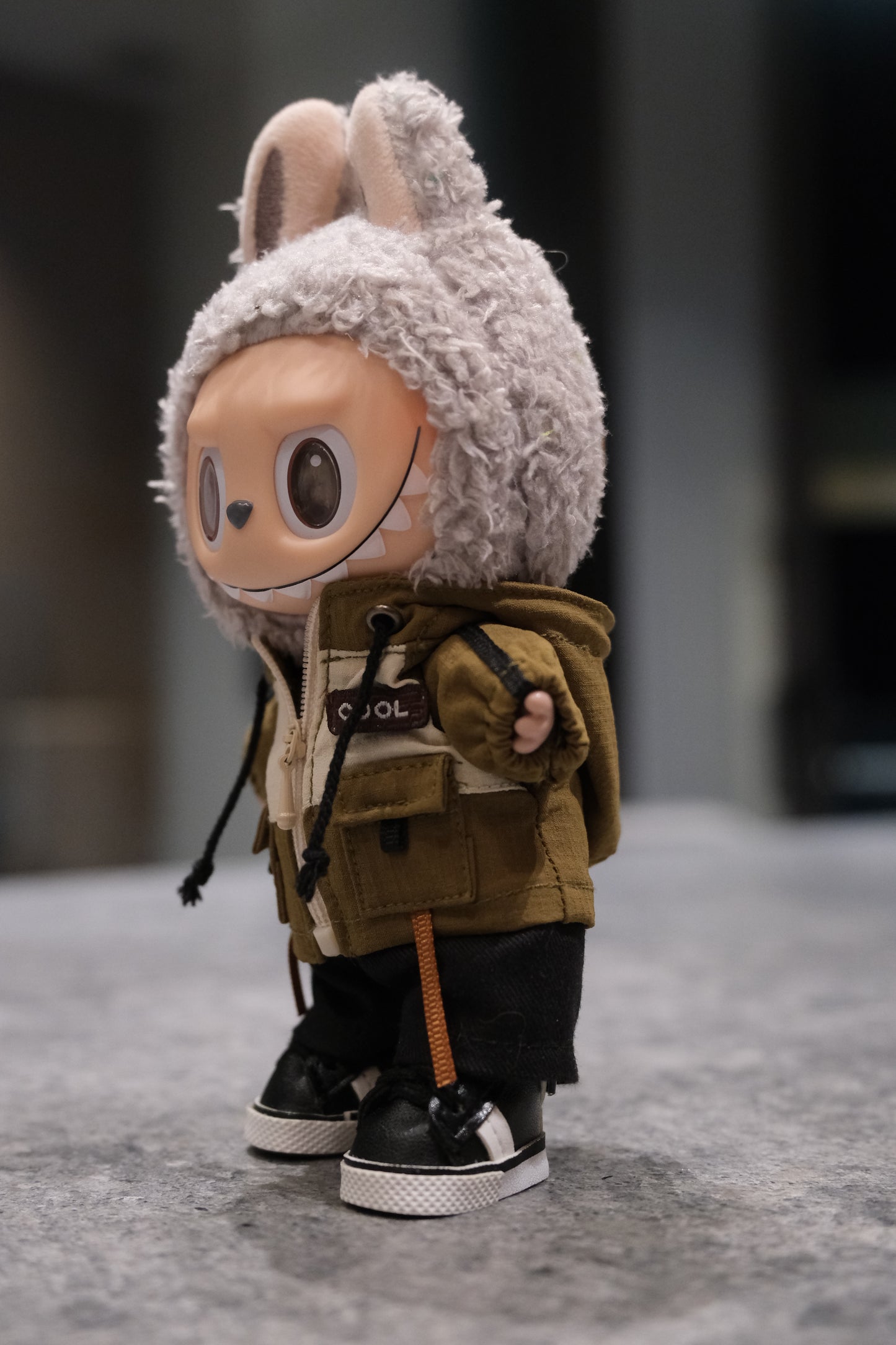 Labubu figure wearing a green and white mountaineering parka jacket, black pants, and black sneakers.