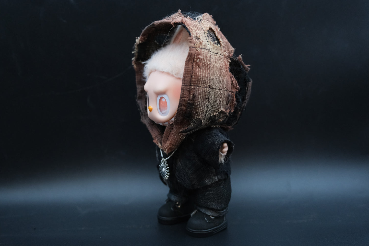 sideview of LABUBU plush doll wearing a distressed black hoodie and a silver sun pendant necklace
