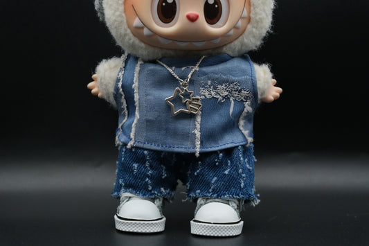 Close-up shot of a Labubu figure showing the frayed edges of the distressed denim vest with visible seams, and the silver necklace with two star-shaped pendants.