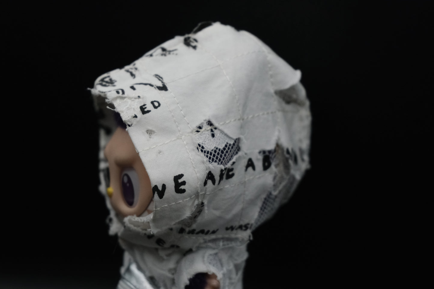 Close-up shot of a Labubu figure showing the layered distressed white graphic hoodie over a ripped white knit top