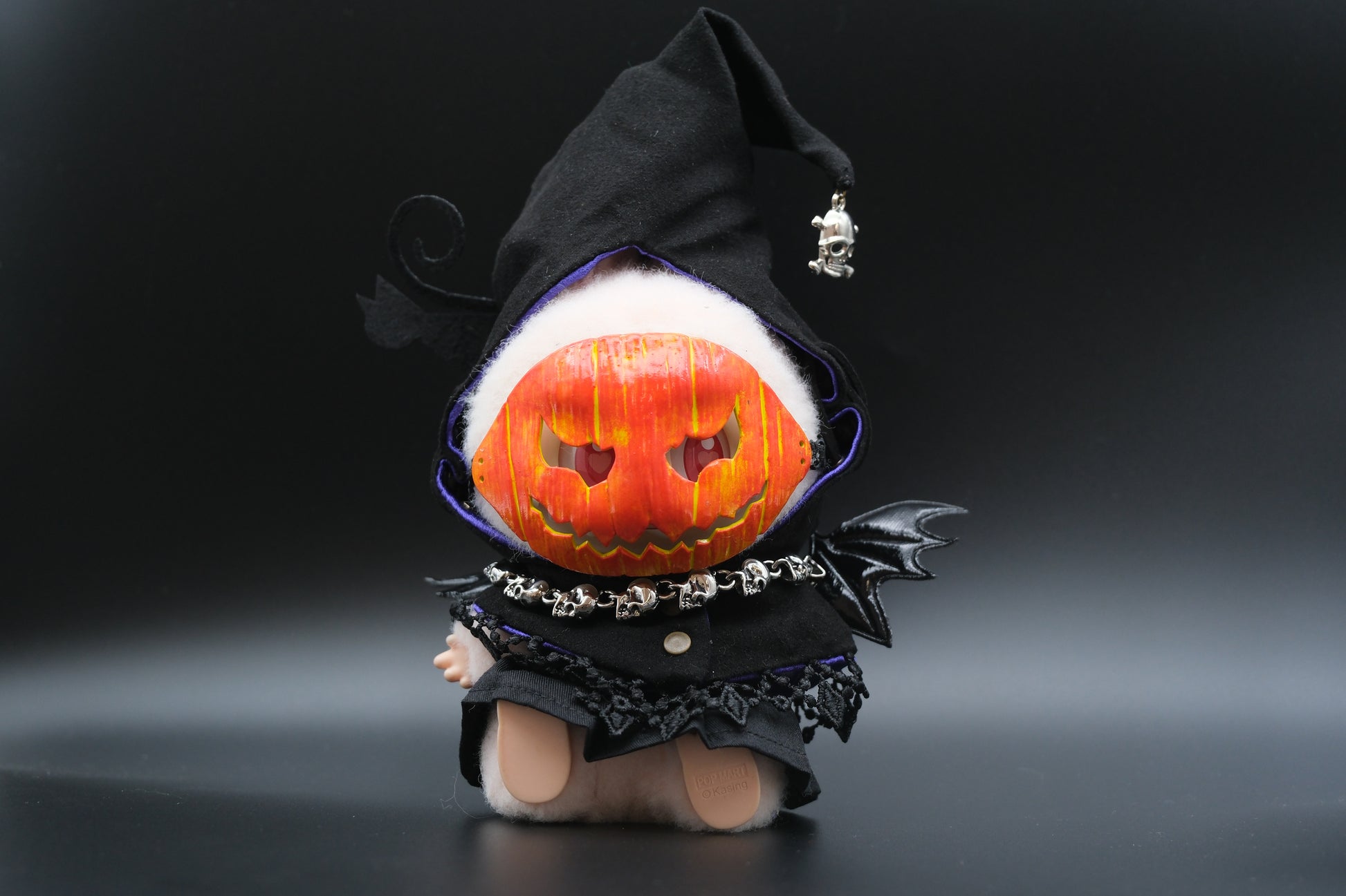 A Labubu figure wearing a 4-piece spooky streetwear outfit, including a black hoodie, a dress, and a pumpkin mask.