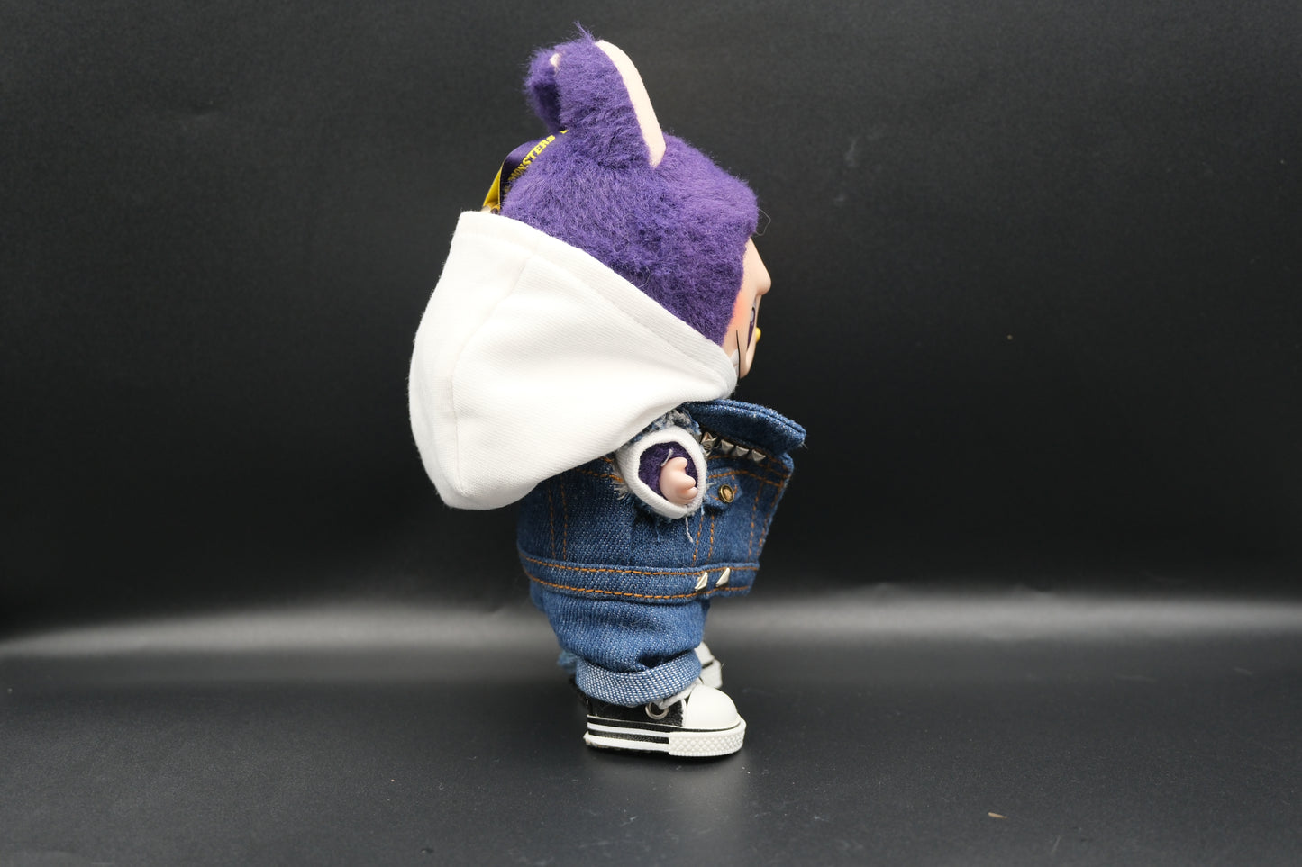 A Labubu designer toy figure showcasing a streetwear look with a white hoodie, a denim jacket, denim jeans and black sneakers.