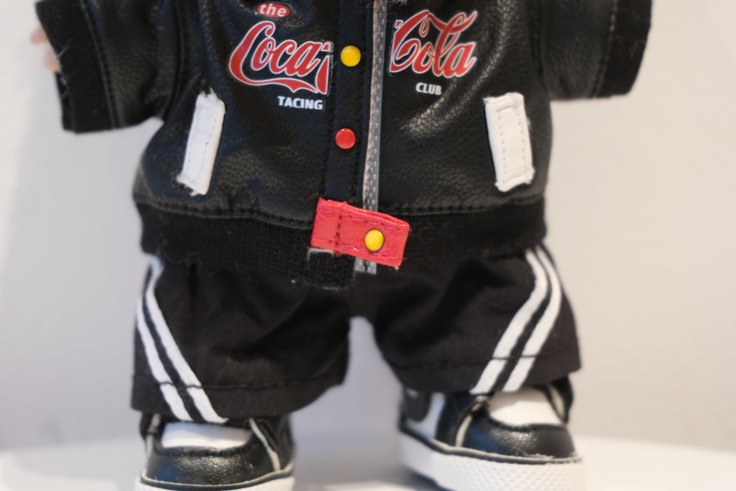 Close-up of The labubu figure's racing jacket with Coca-Cola style logos and white/red detailing