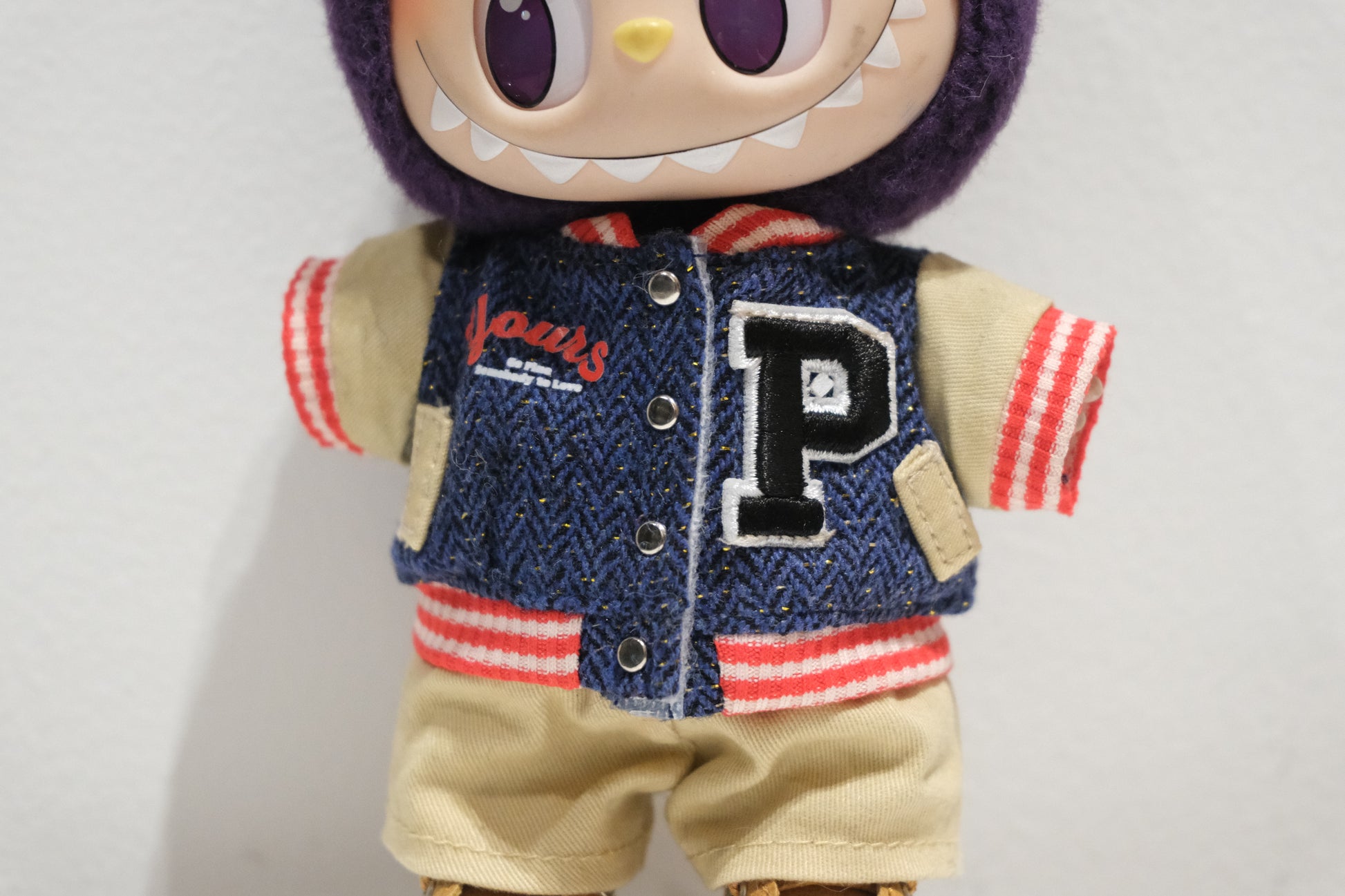 a close up of labubu wearing a varsity jacket with a large letter 'P' 