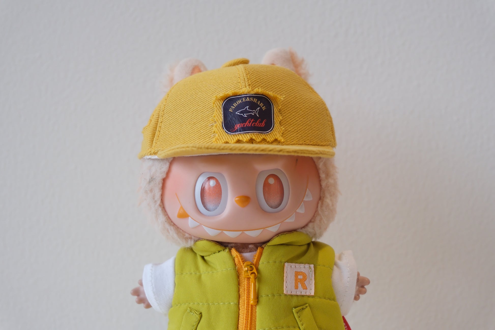 labubu wearing a yellow cap and green vest on a plain background