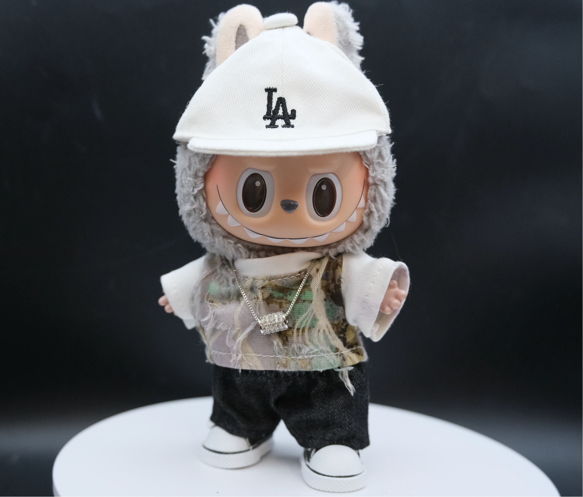 A Labubu figure wearing a streetwear outfit with a distressed camouflage T-shirt, a white LA baseball cap, and white sneakers