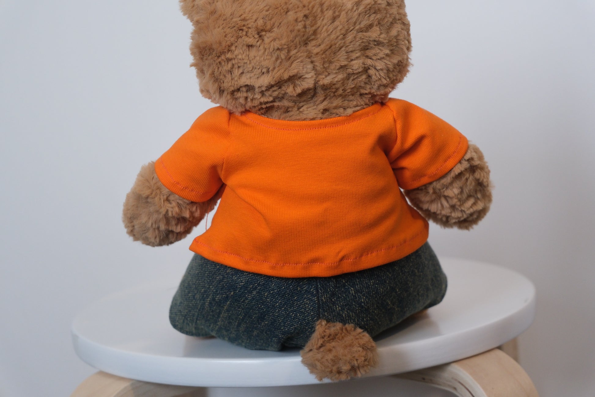back view Jellycat Bartholomew Bear plush wearing a classic 2-piece outfit with a white T-shirt and blue denim jeans.