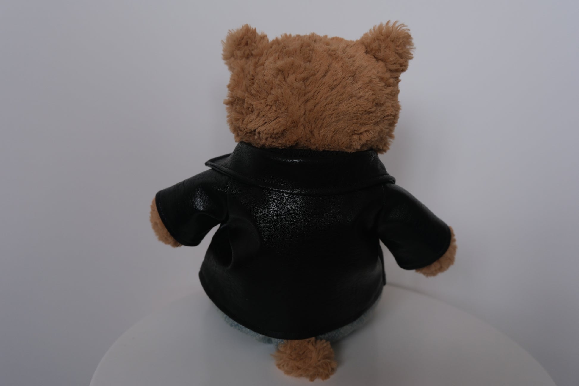 Jellycat Bartholomew Bear wearing a 3-piece punk outfit including a black leather jacket, black sweater, and denim jeans.