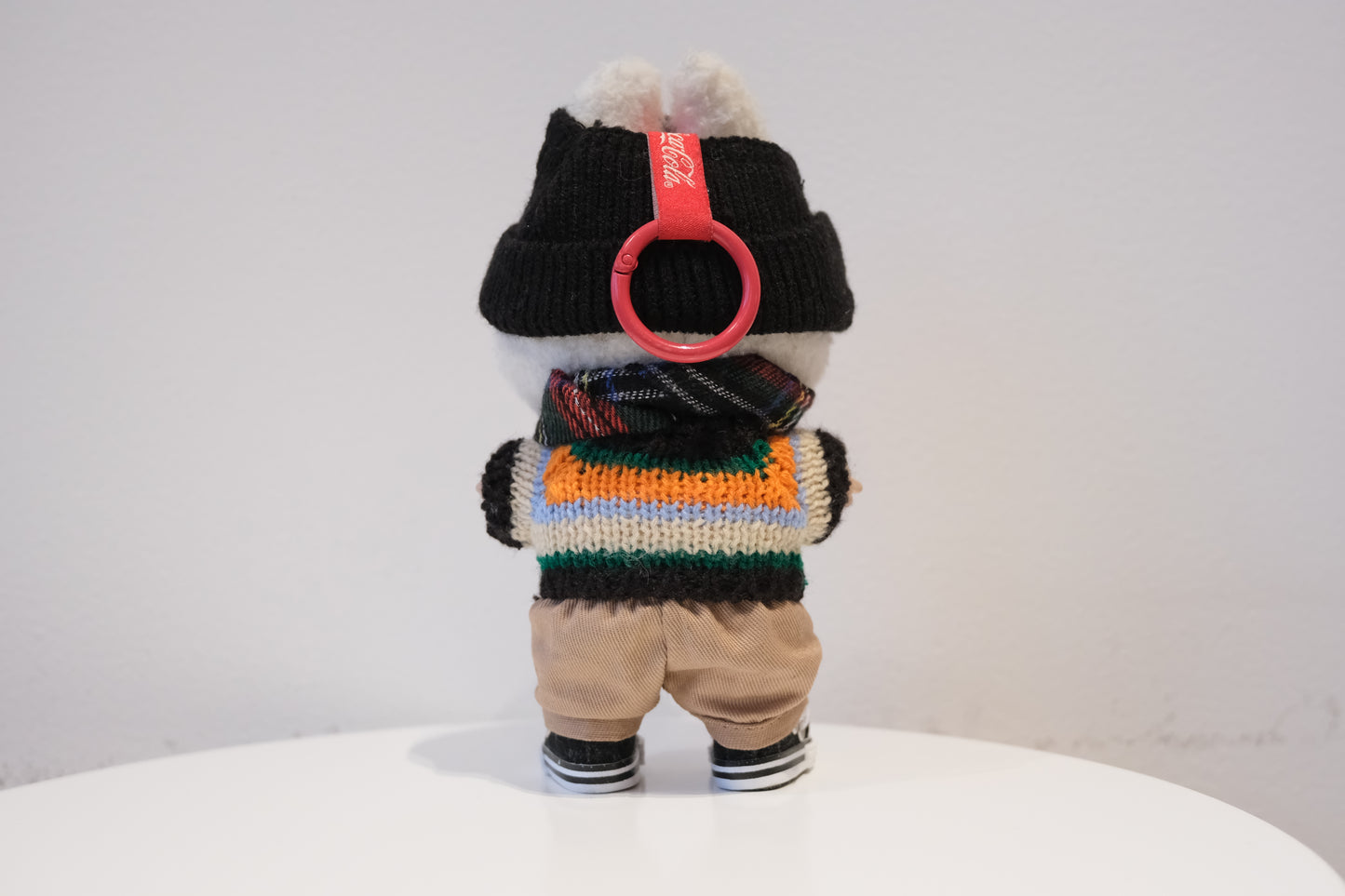 back view of Labubu figure wearing a 5-piece preppy streetwear outfit with a black and white Argyle sweater, black beanie, scarf, and sneakers.