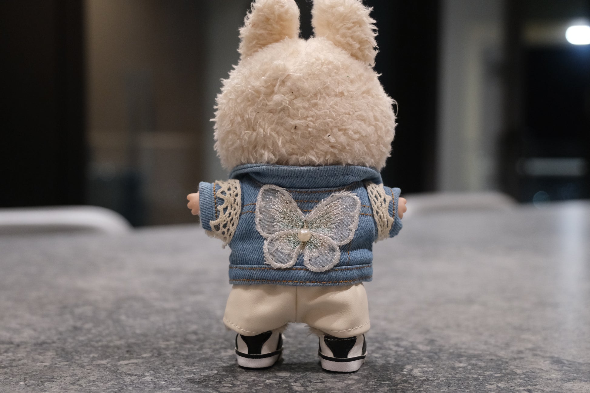 Labubu figure wearing a 5-piece outfit: light blue denim jacket, white tee, white leather shorts, sun necklace, and sneakers.
