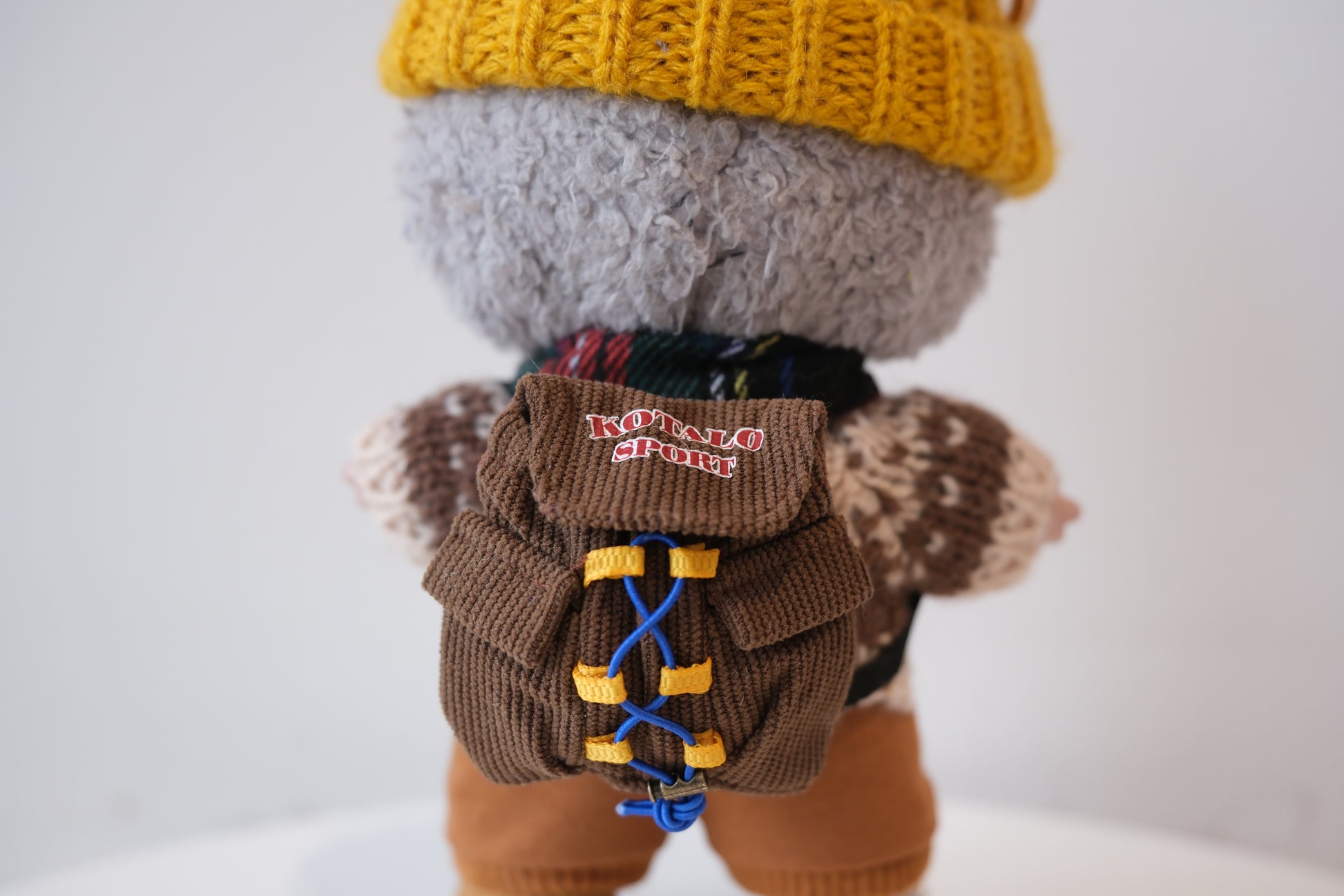 labubu wearing a yellow hat and brown backpack with blue laces on a white background