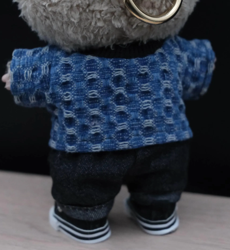 Labubu wearing a blue sweater and dark pants on a wooden surface.