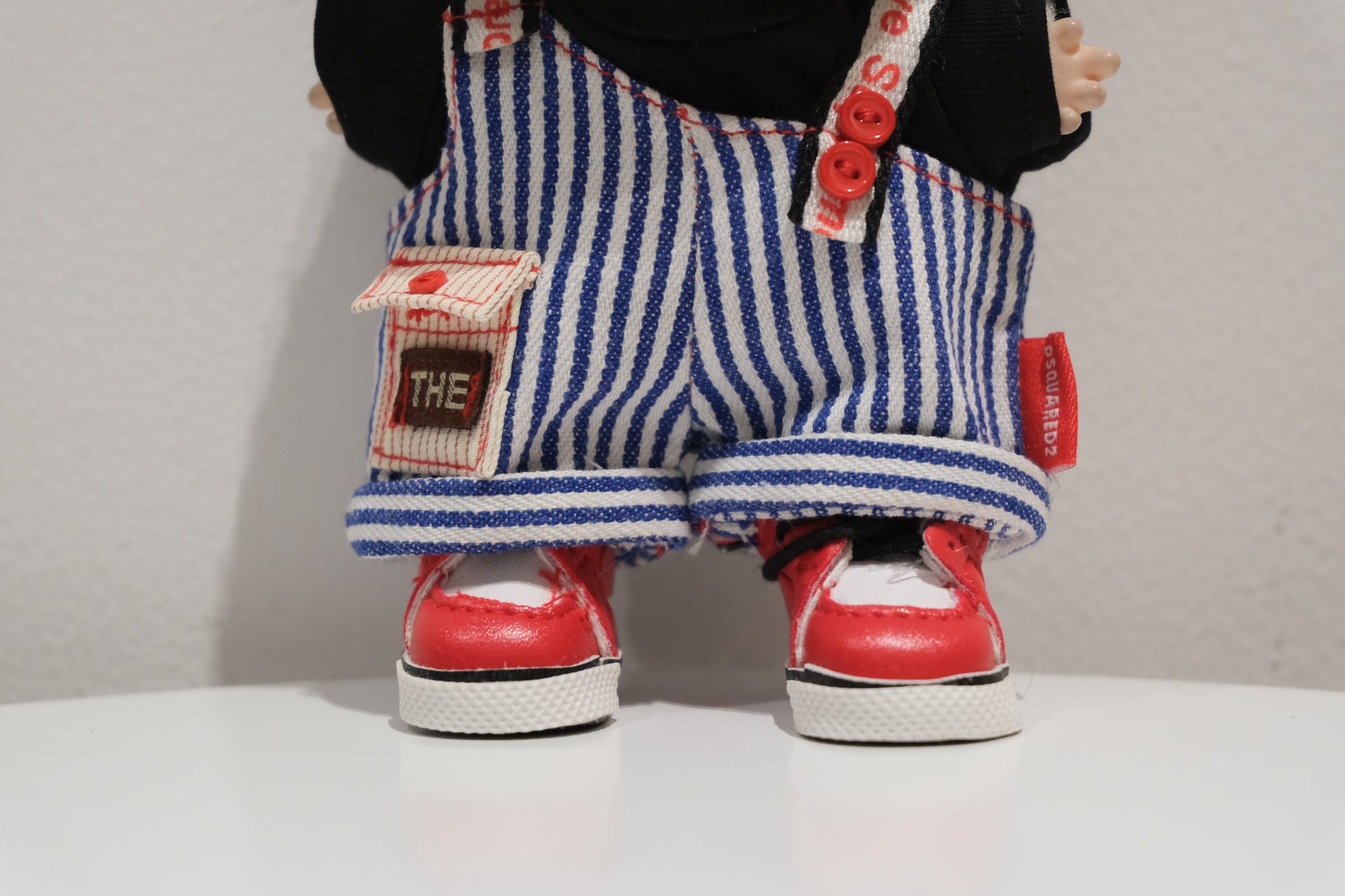 Close-up of The labubu figure in the pinstripe dungarees and black t-shirt