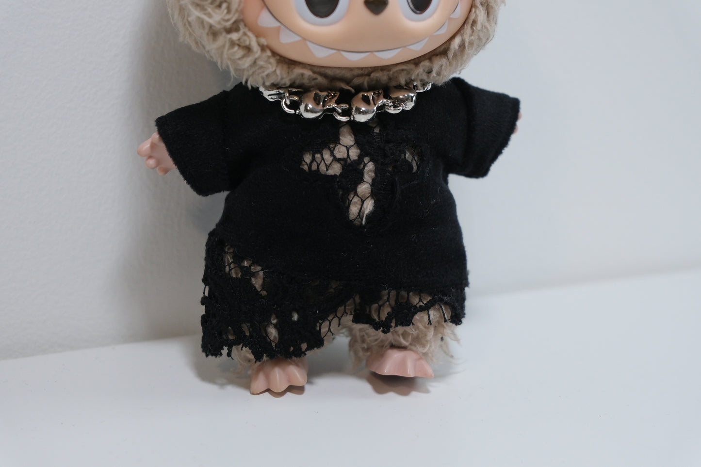 a close up pf Labubu figure wearing a black goth dress with lace/shredded hem and a chunky skull chain necklace