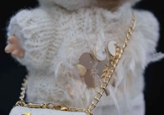 Close-up of a labubu wearing a white knitted sweater with a gold chain and butterfly design.