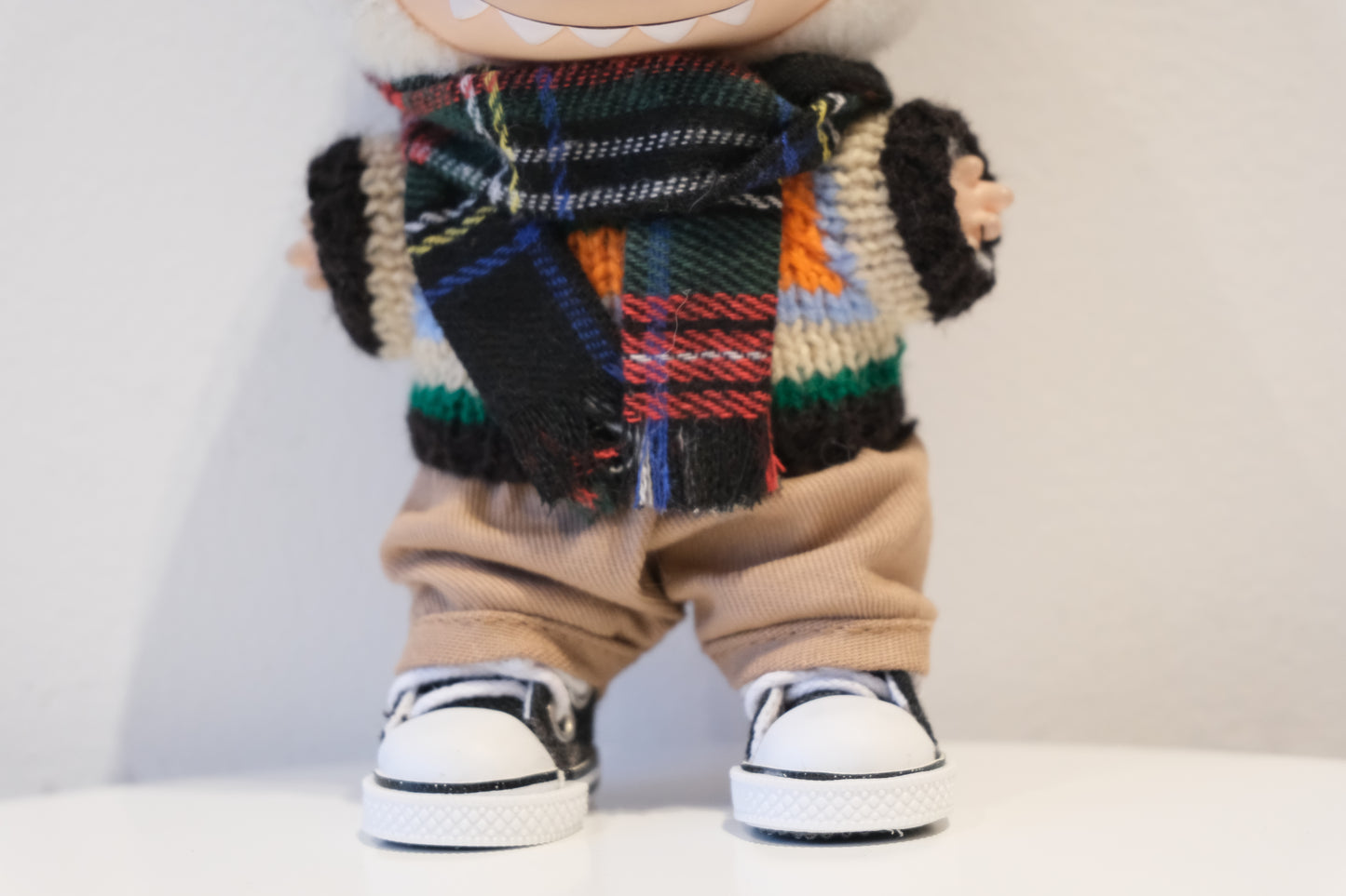 labubu wearing a colorful scarf, beige pants, and black and white shoes 